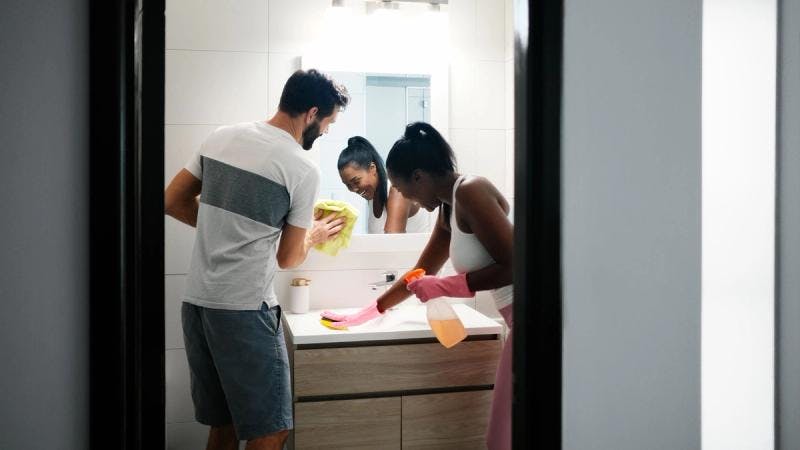 Un couple nettoie une évier et un miroir dans une salle de bain.