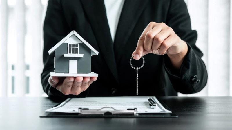 Une personne se tenant devant un contrat tient une clé dans une main et une maison miniature dans l’autre