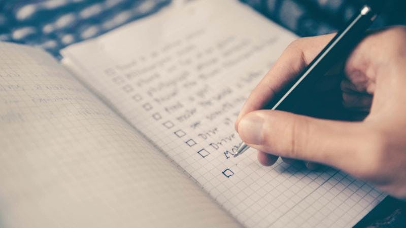 Une personne écrit une liste de tâches dans un carnet.